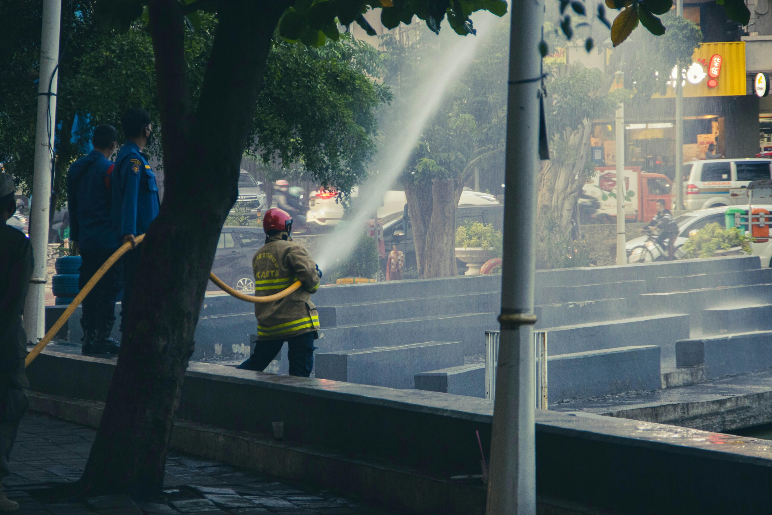 Firefighters using a hose to combat a fire with police observing in an urban setting.