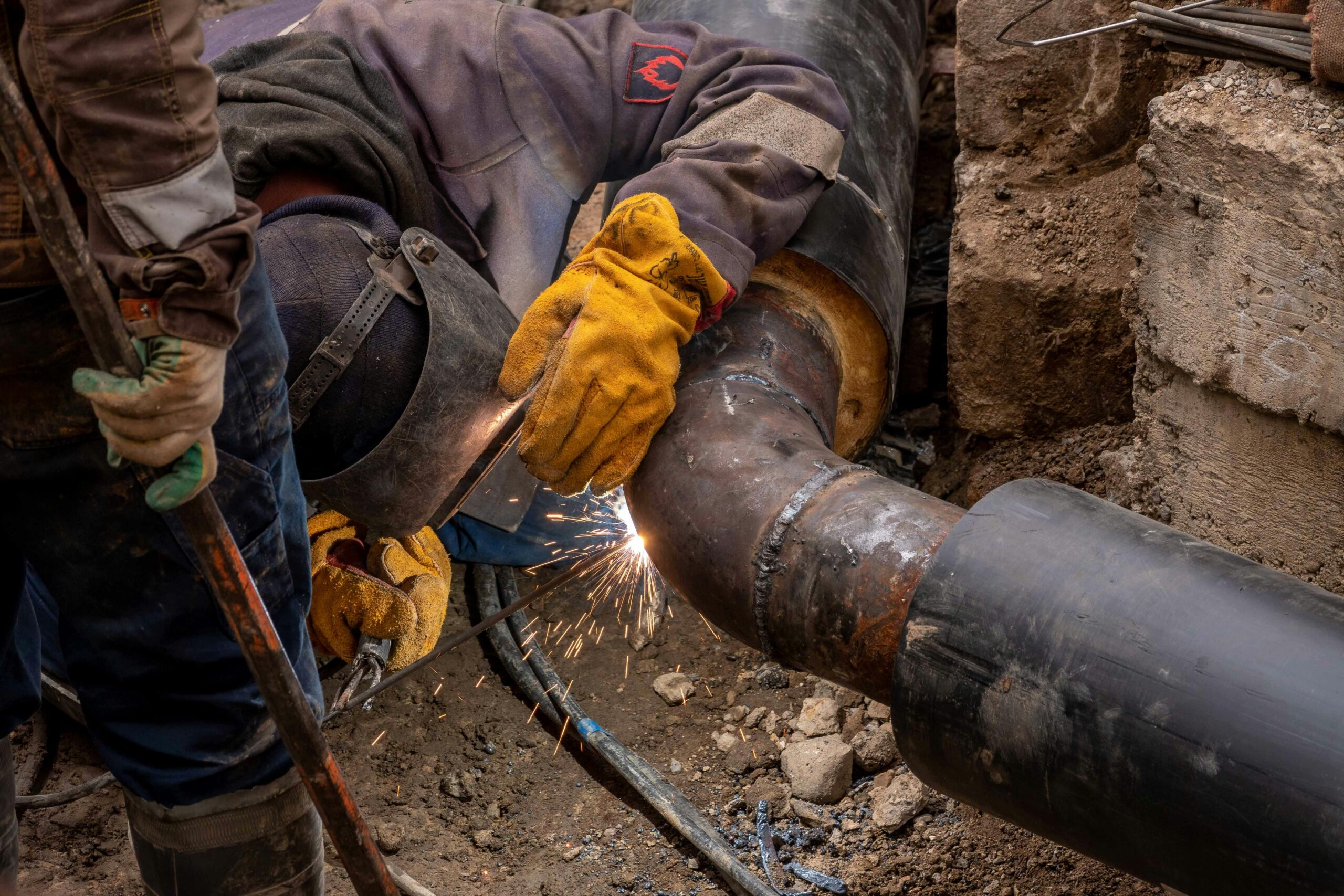 Close-up of a skilled worker welding a steel pipe outdoors at a construction site.